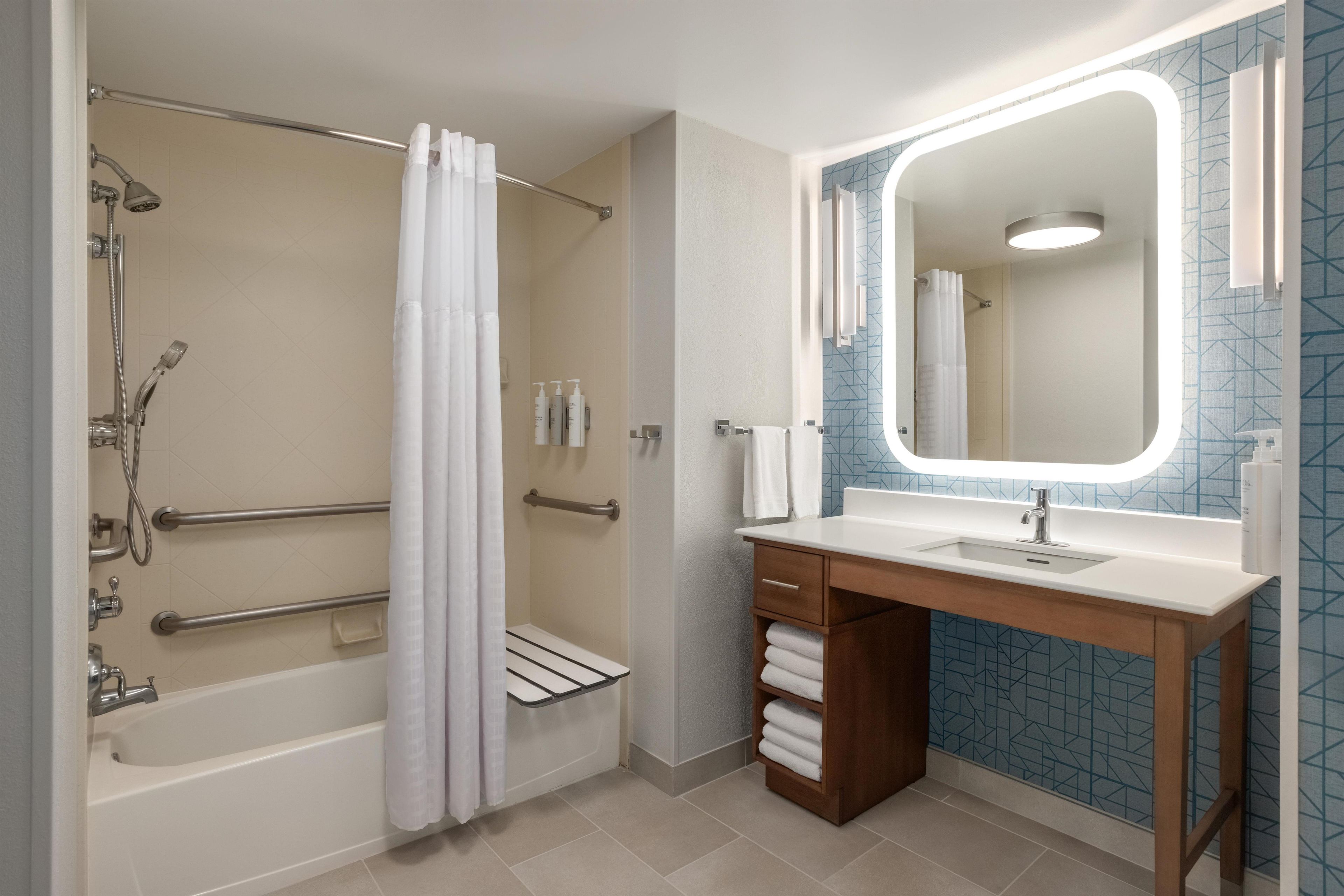 Une salle de bain moderne dotée d’une douche à l’italienne, de barres d’appui, d’un meuble-lavabo avec miroir et d’un porte-serviettes.