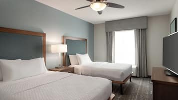 A hotel room with two beds, a ceiling fan, a TV, and a large window with curtains.