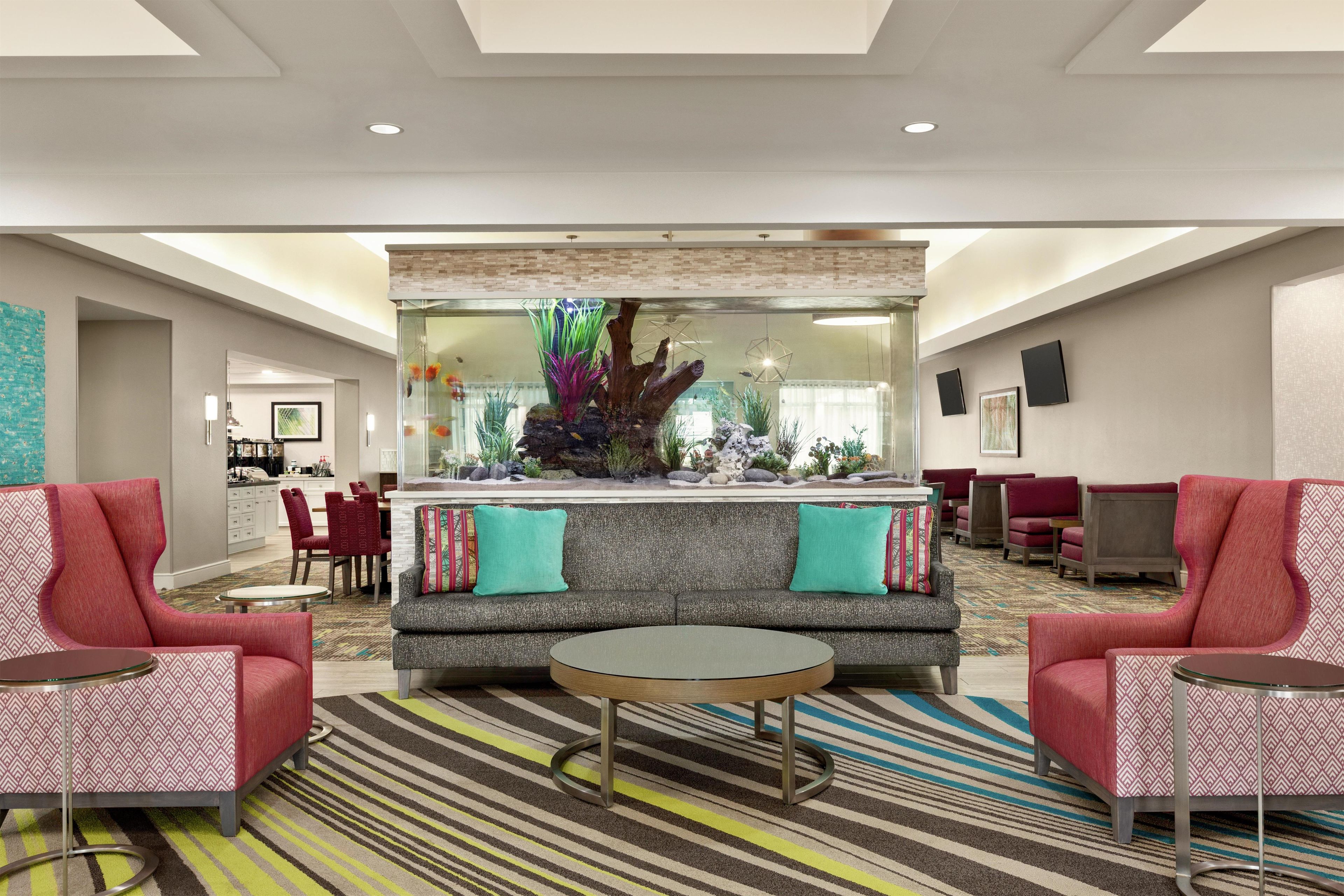 A lobby with a sofa, two armchairs, a coffee table, a fish tank, and a dining area.