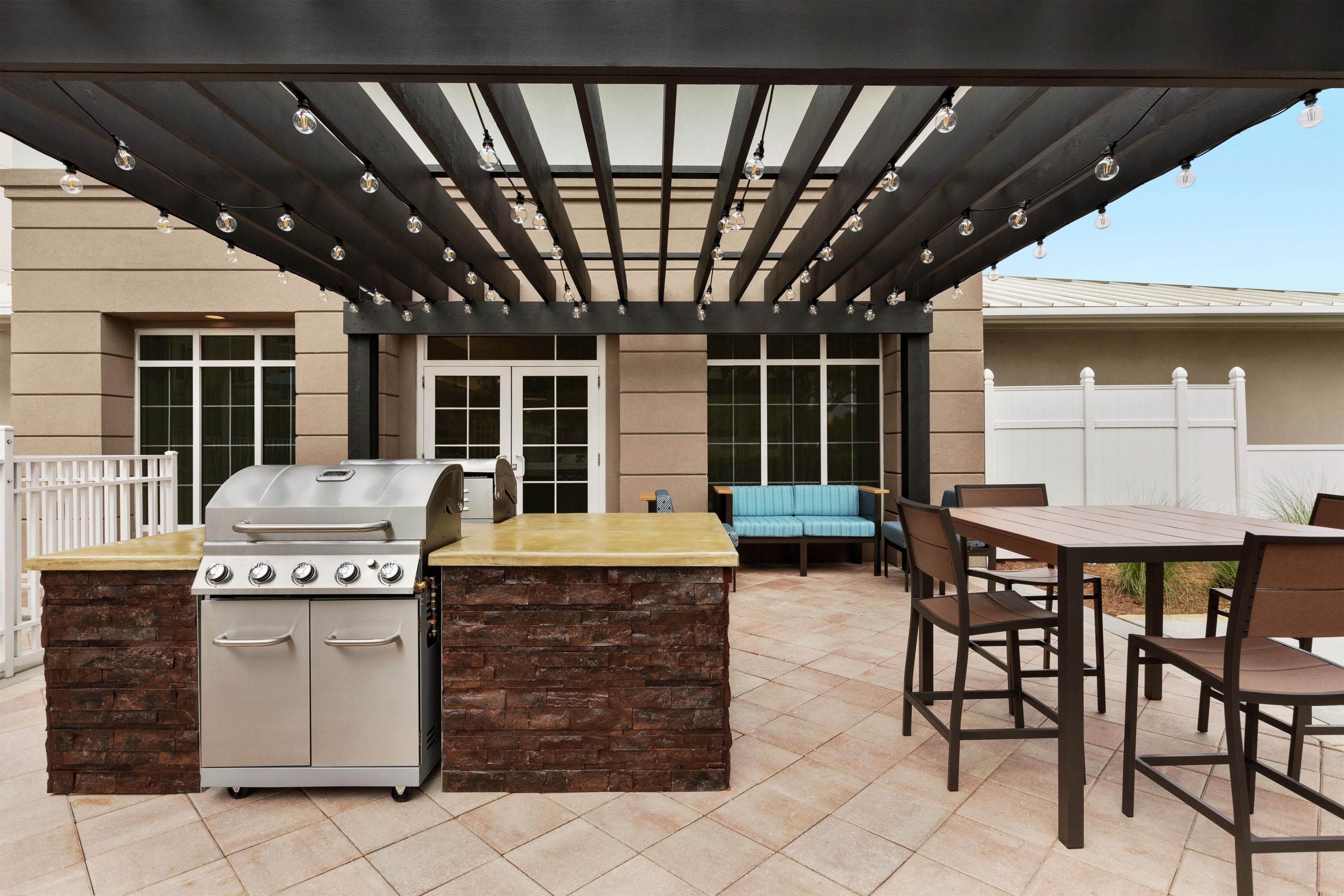 An outdoor patio with a grill, dining table, and chairs.