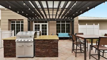 An outdoor patio with a grill, dining table, and chairs.