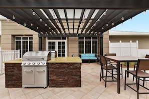 An outdoor patio with a grill, dining table, and chairs.