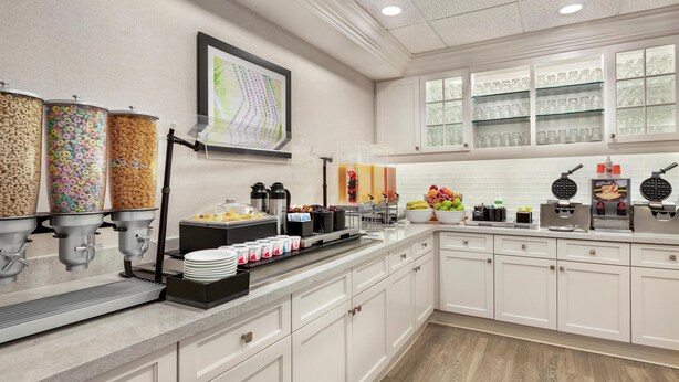 A modern kitchen with a breakfast bar, cereal dispensers, a fruit bowl, and a waffle maker.