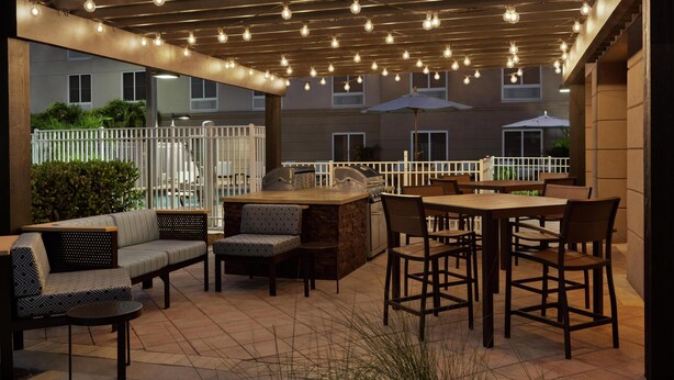 Un patio exterior con zona de barbacoa, asientos e iluminación con guirnaldas.