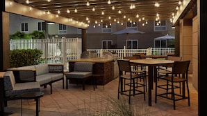 An outdoor patio with a barbecue area, seating, and string lights.