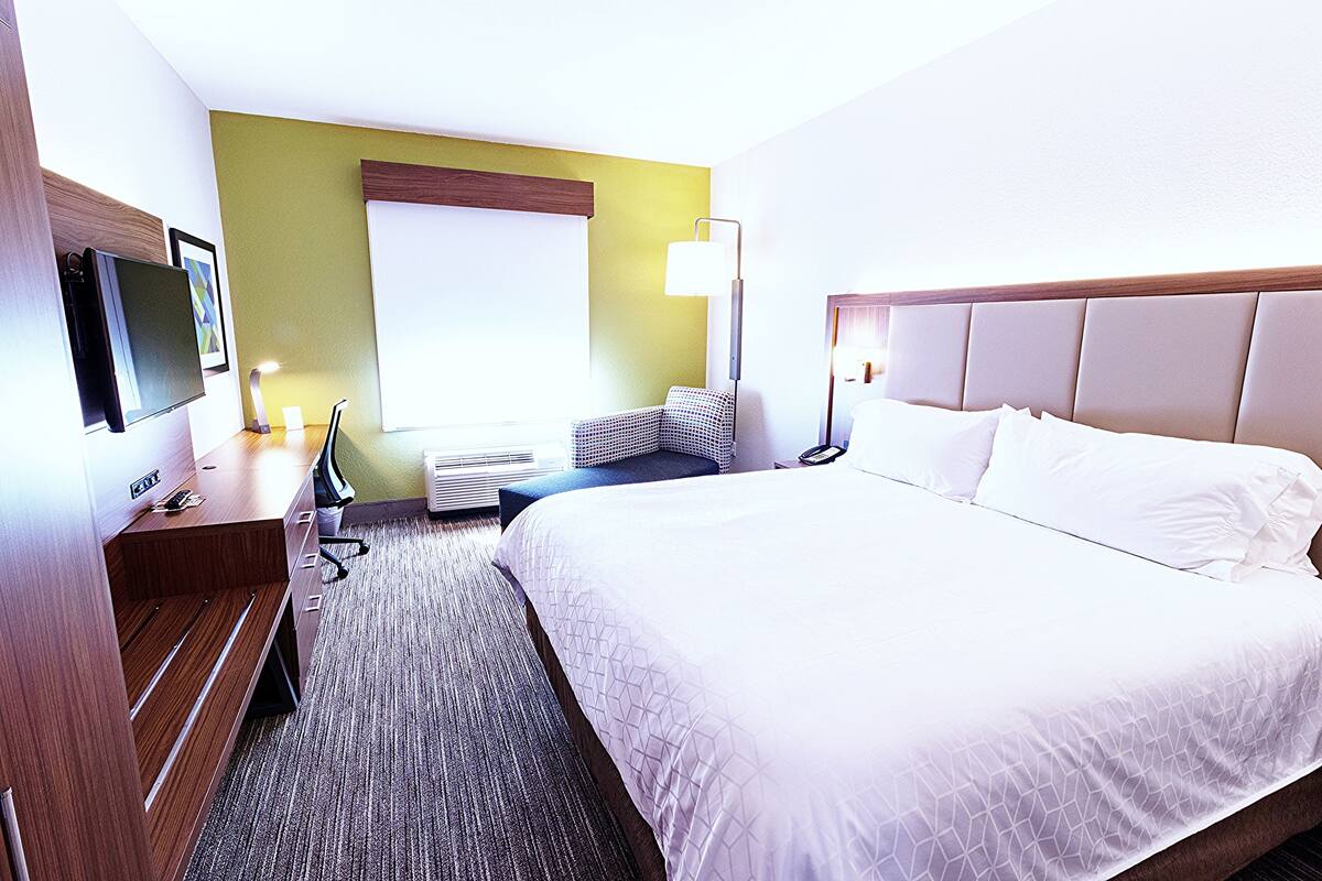 A hotel room with a large bed, a desk with a computer, a chair, and a TV.