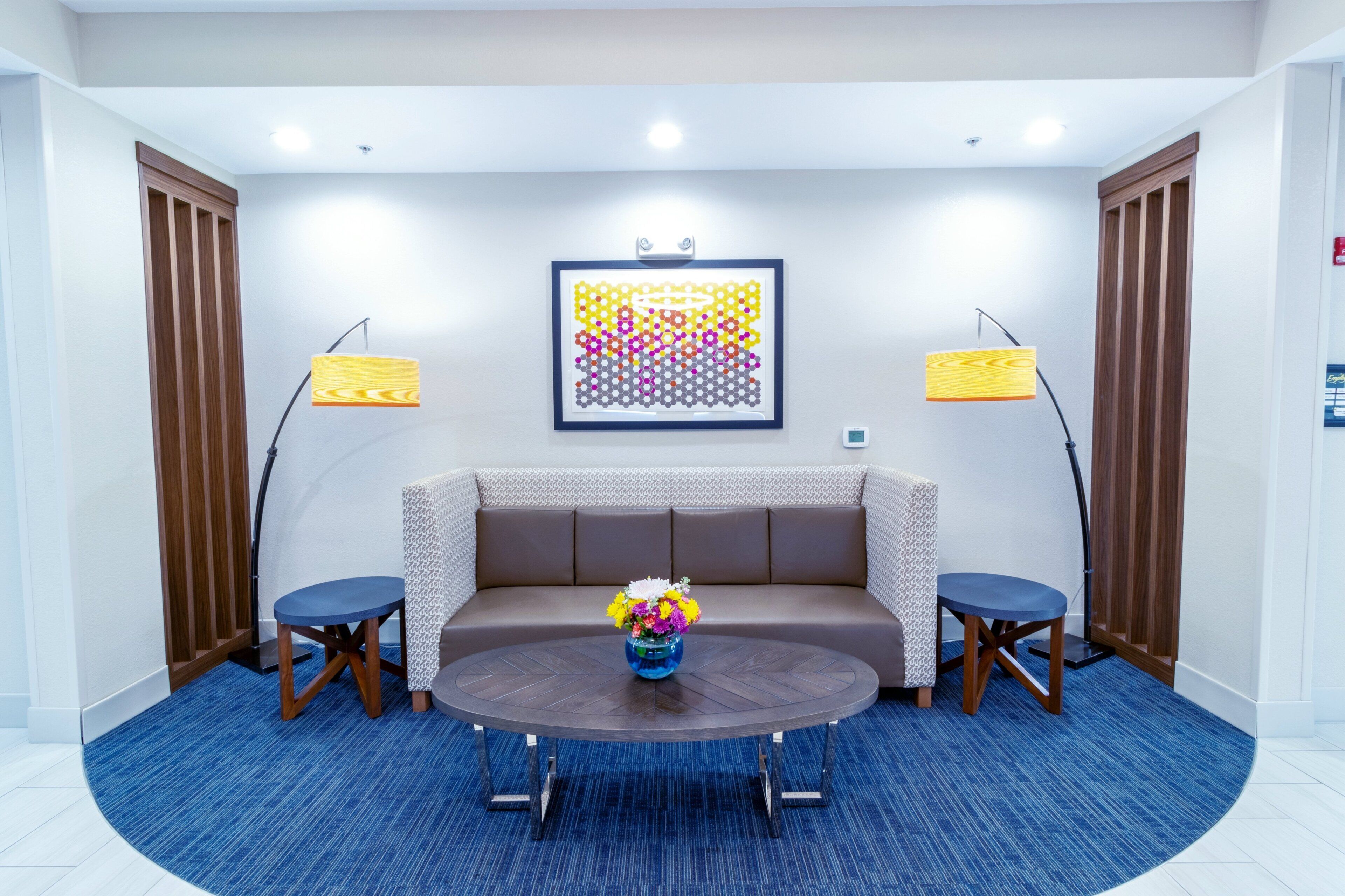 Quarto moderno com sofá marrom, duas poltronas, mesa de centro redonda e um quadro abstrato colorido na parede.
