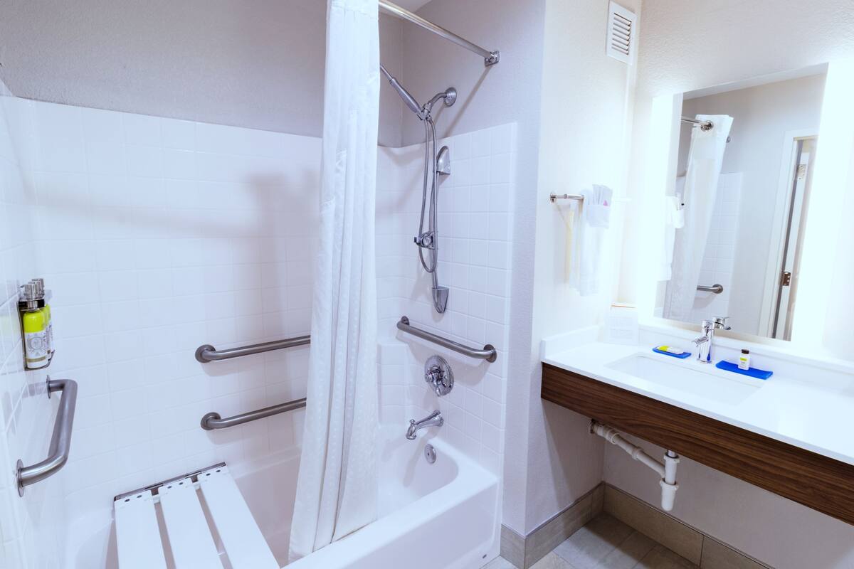 A modern bathroom with a shower, grab bars, a sink, and a mirror.