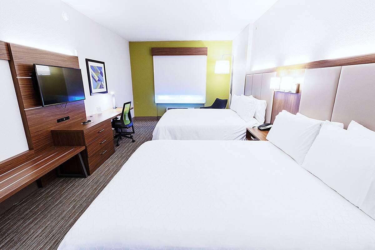 A hotel room with two beds, a TV, a desk with a chair, and a window with a view.