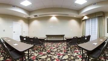 Un salón de conferencias con una larga mesa y sillas, piso alfombrado y una puerta blanca.