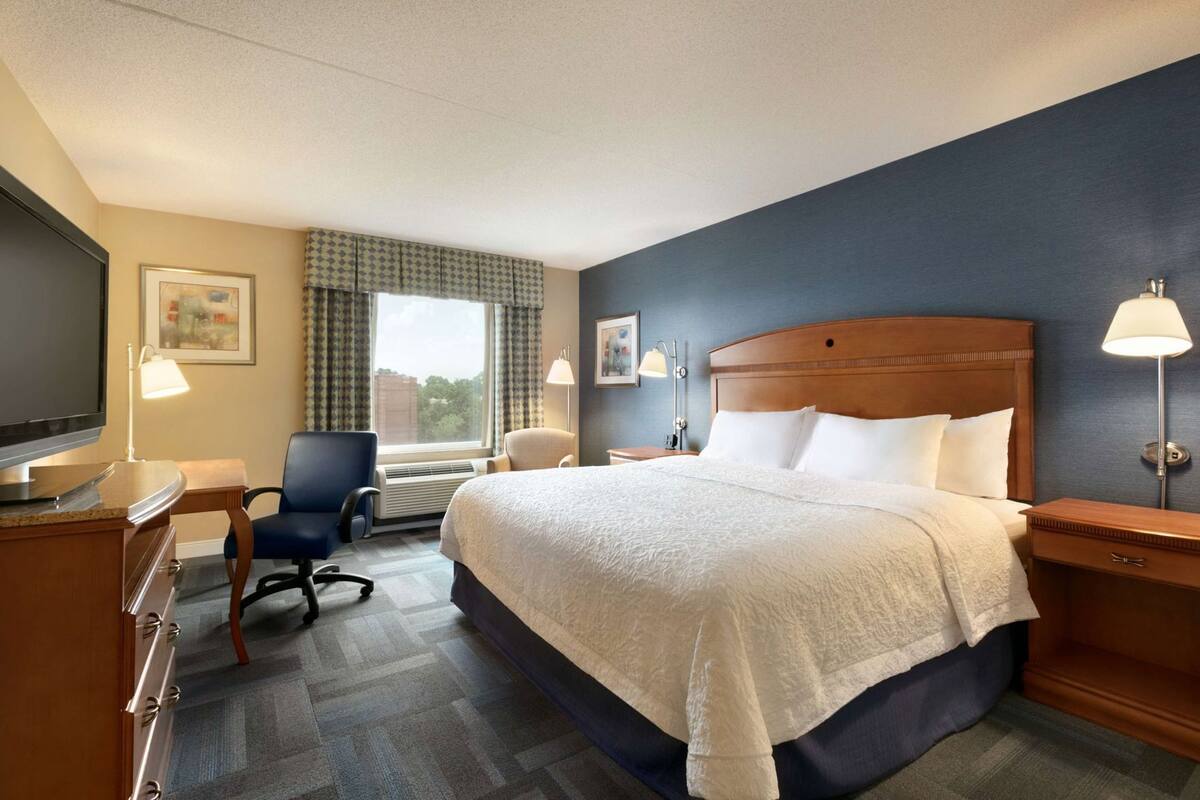 Une chambre d’hôtel équipée d’un lit, d’un bureau, d’une chaise, d’une télévision et de deux lampes de chevet.