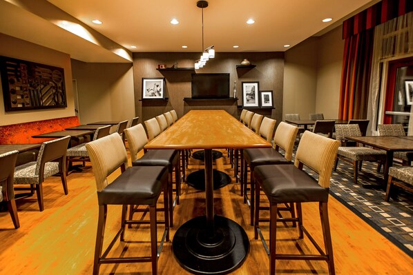A conference room with a large wooden table surrounded by chairs, a television, and framed pictures on the walls.