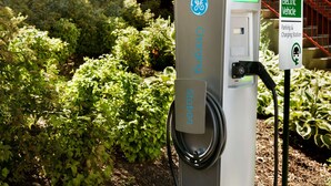Een laadstation voor elektrische voertuigen met een GE logo, een bord dat aangeeft dat het voor elektrische voertuigen is, en een parkeersbord.