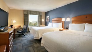 Hotelkamer met twee bedden, een bureau, een stoel, een televisie en een raam met gordijnen.