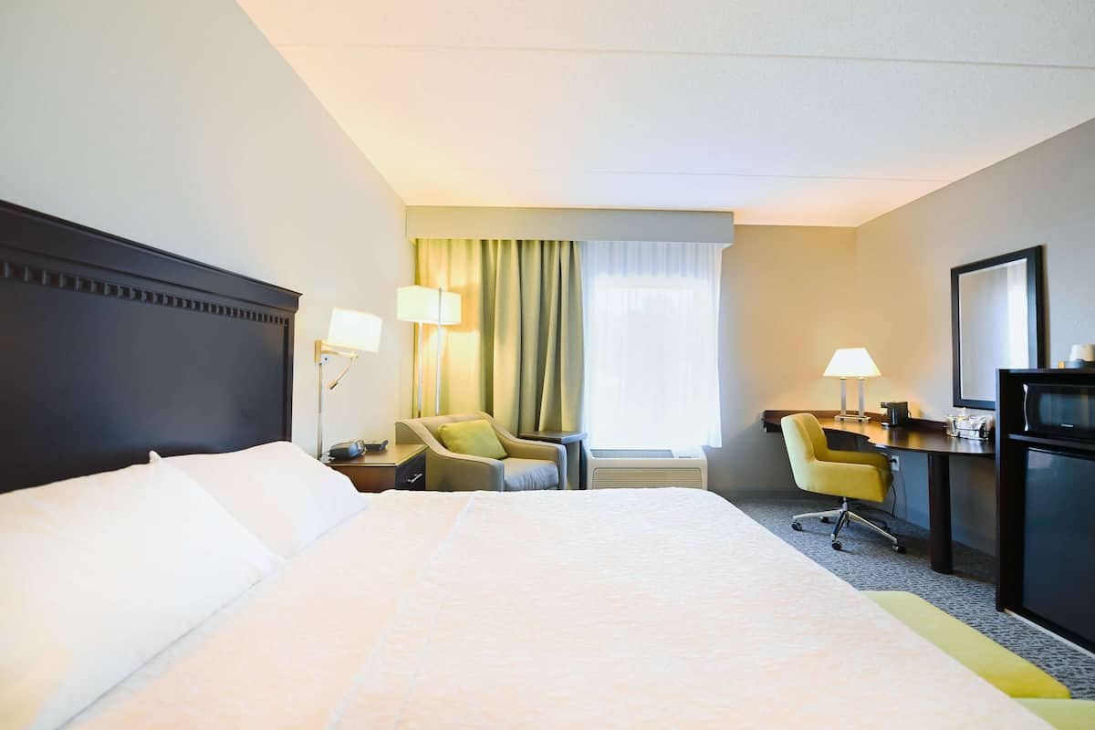 A hotel room with a large bed, two chairs, a desk with a computer, and a television.