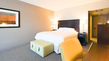 A hotel room with a bed, bedside tables, a chair, a small table, and a framed picture on the wall.