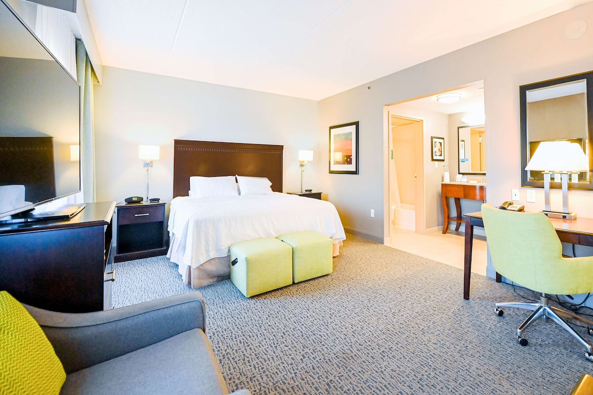 A hotel room with a bed, bedside tables, a desk, a chair, and a bathroom visible through an open door.
