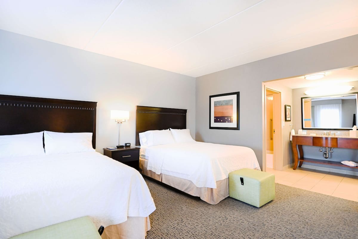 A hotel room with two beds, a bathroom with a vanity, and a framed picture on the wall.