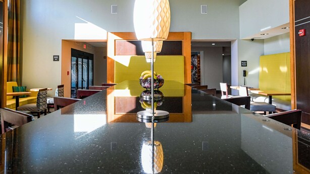 Un moderno vestíbulo de hotel con una zona de bar central, arreglos de asientos y un accesorio de iluminación decorativo.