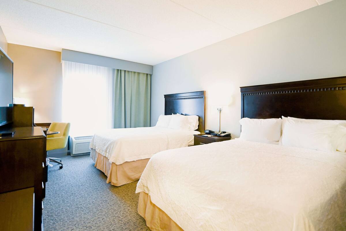 A hotel room with two beds, a desk, a chair, and a television.