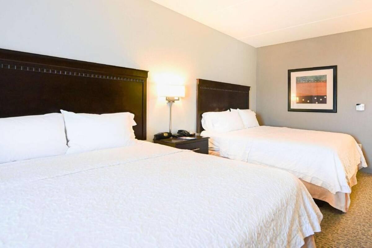 A hotel room with two beds, a nightstand with a lamp, and a framed picture on the wall.