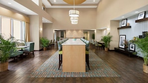 A spacious lobby with a central island table, seating, and potted plants.