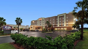 A Hampton Inn & Suites by Hilton hotel with a parking lot, palm trees, and a clear sky.