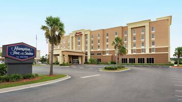 A Hampton Inn & Suites by Hilton building with a parking lot and palm trees.