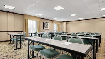 A conference room with multiple tables and chairs, a patterned carpet, and a ceiling with fluorescent lights.