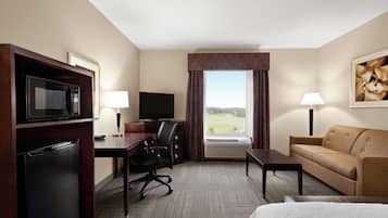 Habitación de hotel con cama, escritorio con computadora, microondas, televisor, sofá y ventana con vista al exterior.