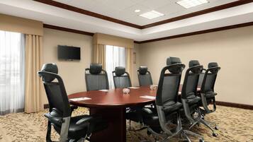 A conference room with a large table, eight chairs, a television on the wall, and large windows with curtains.