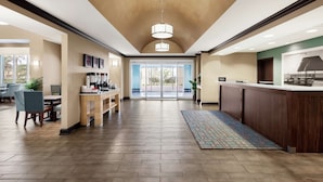 A spacious lobby with a high ceiling, a reception desk, seating area, and a view through the glass doors.