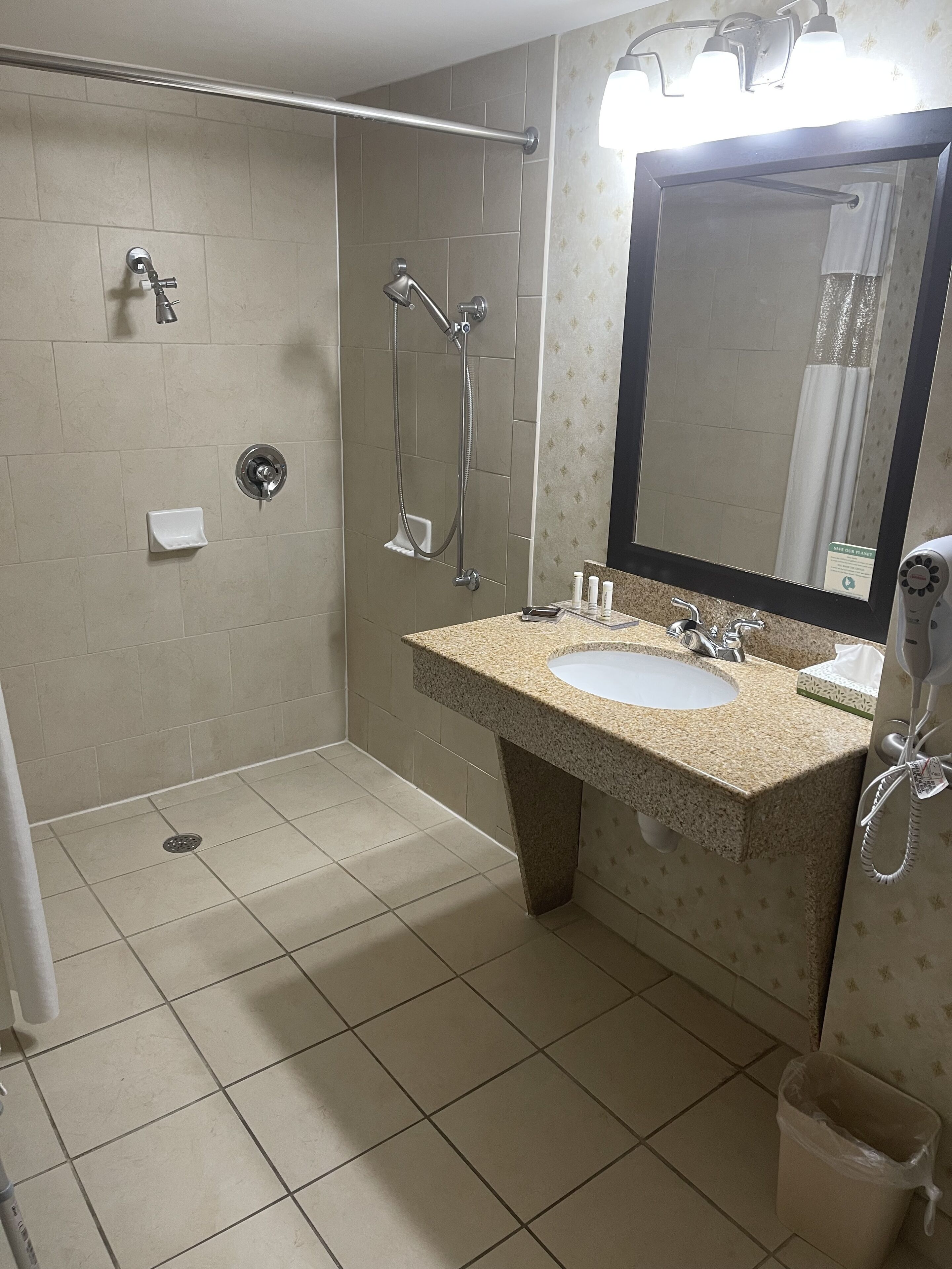Une salle de bain équipée d’une douche, d’un lavabo, d’un miroir et d’un sèche-mains.