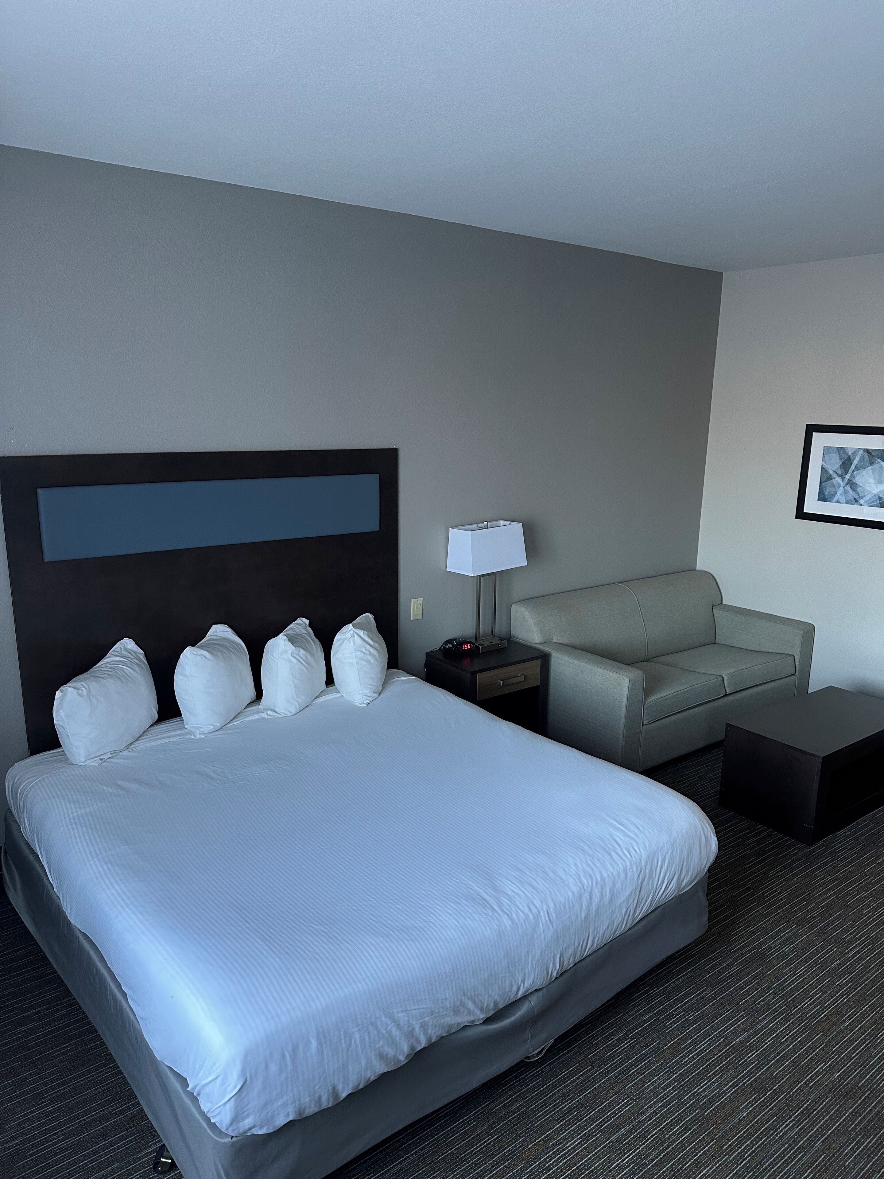 A hotel room with a large bed, a grey sofa, a small table, and a nightstand.