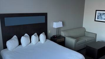 A hotel room with a large bed, a grey sofa, a small table, and a nightstand.