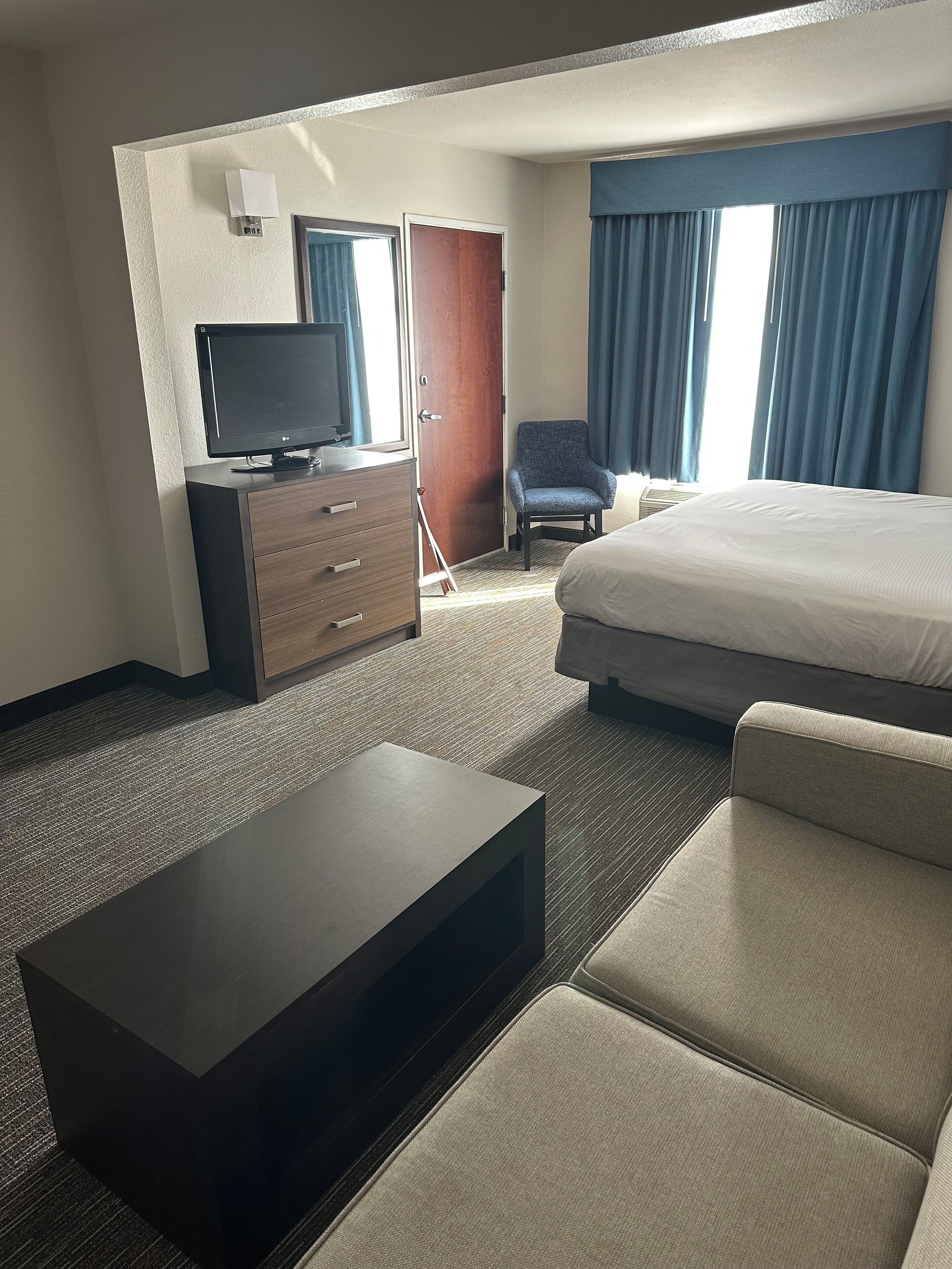 Ein Hotelzimmer mit Bett, Fernseher, Schreibtisch, Stuhl und einem Fenster mit Vorhängen.