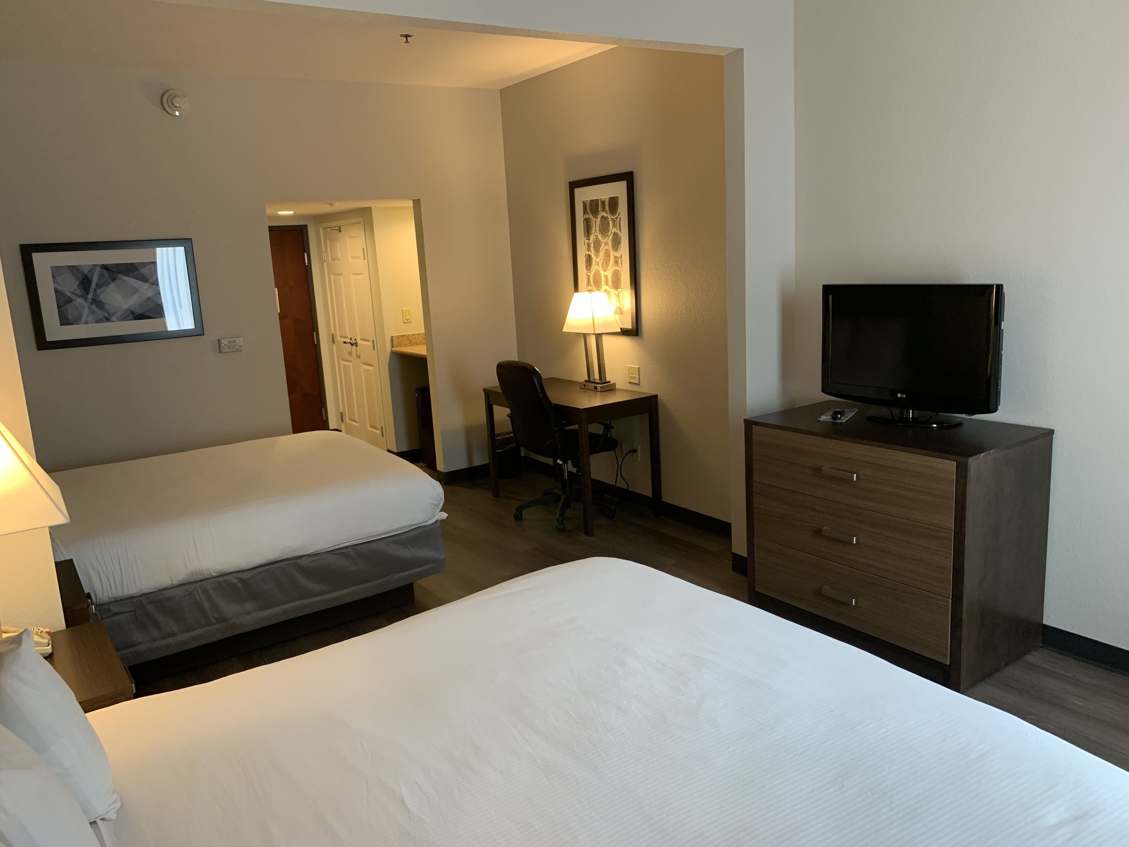 Hotellihuone, jossa on kaksi sänkyä, työpöytä tuolilla, televisio ja lamppu.