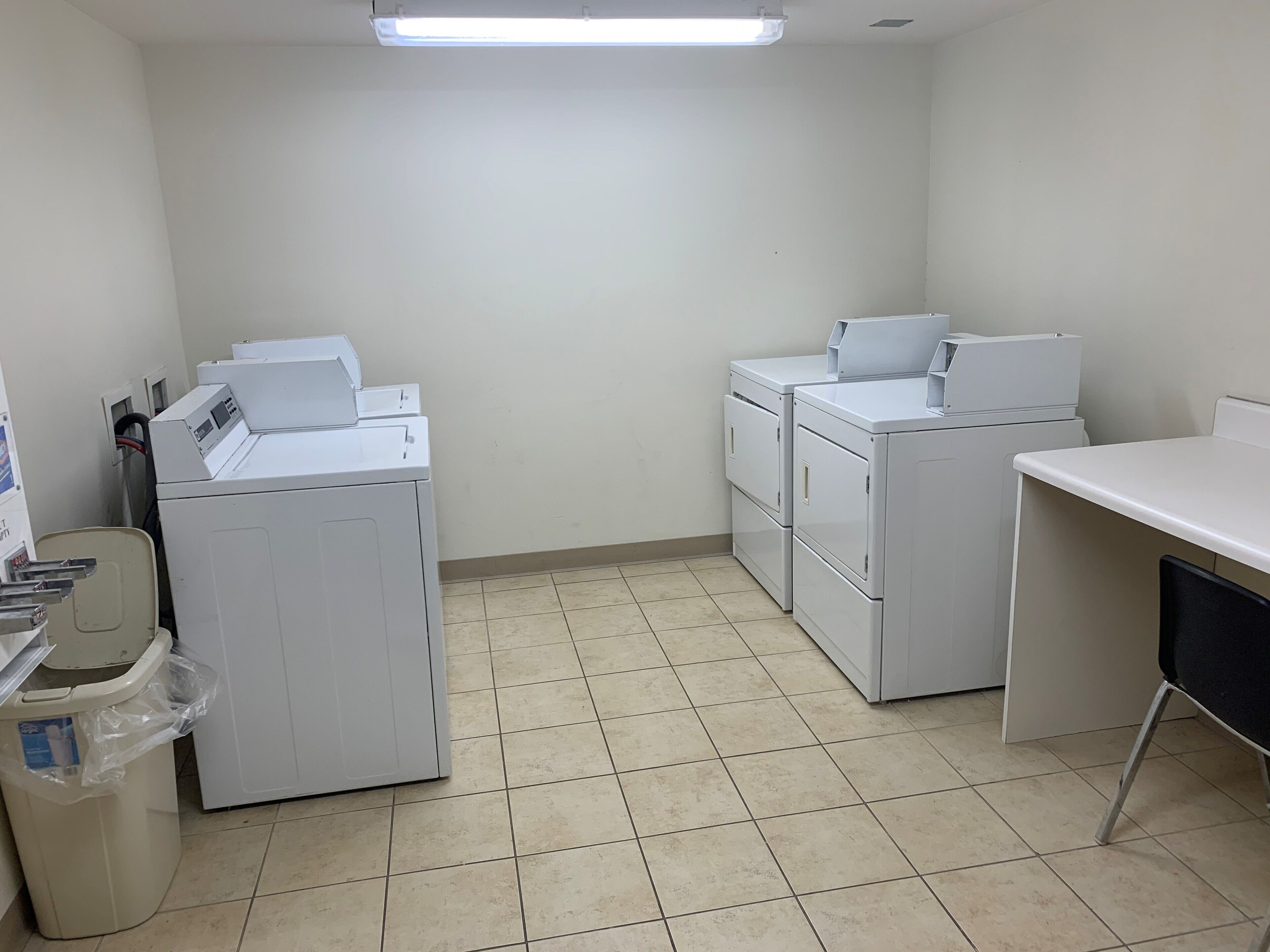 Una sala de bugaderia amb piles de rentadores i assecadores, un safataire i un sòl de rajola.