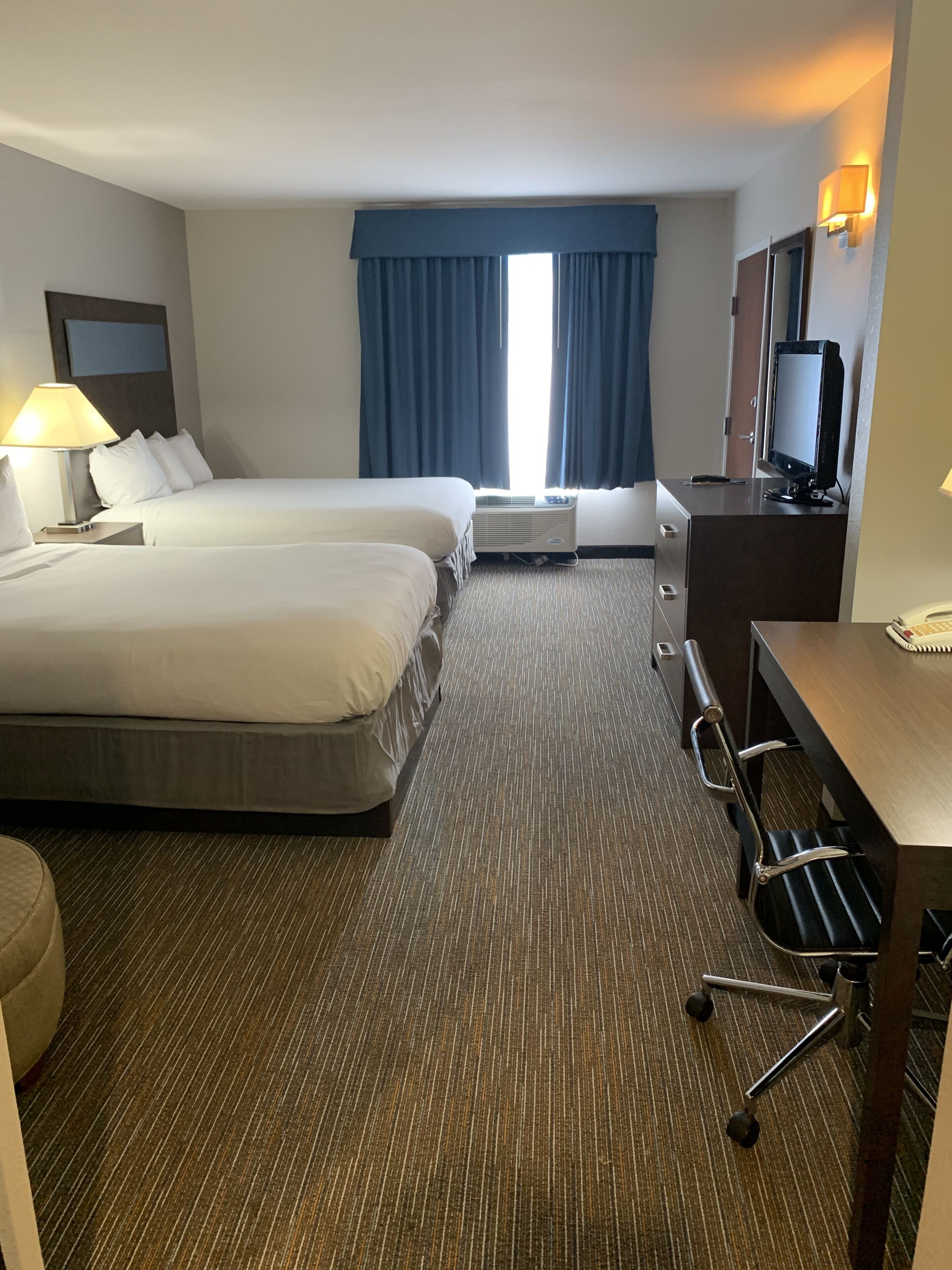 A hotel room with two beds, a desk, a chair, a TV, and a window with curtains.