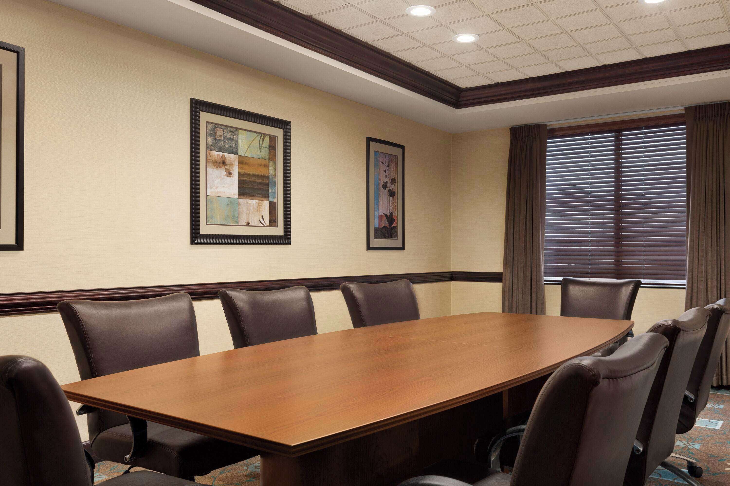 A conference room with a long wooden table, six leather chairs, and framed artwork on the walls.