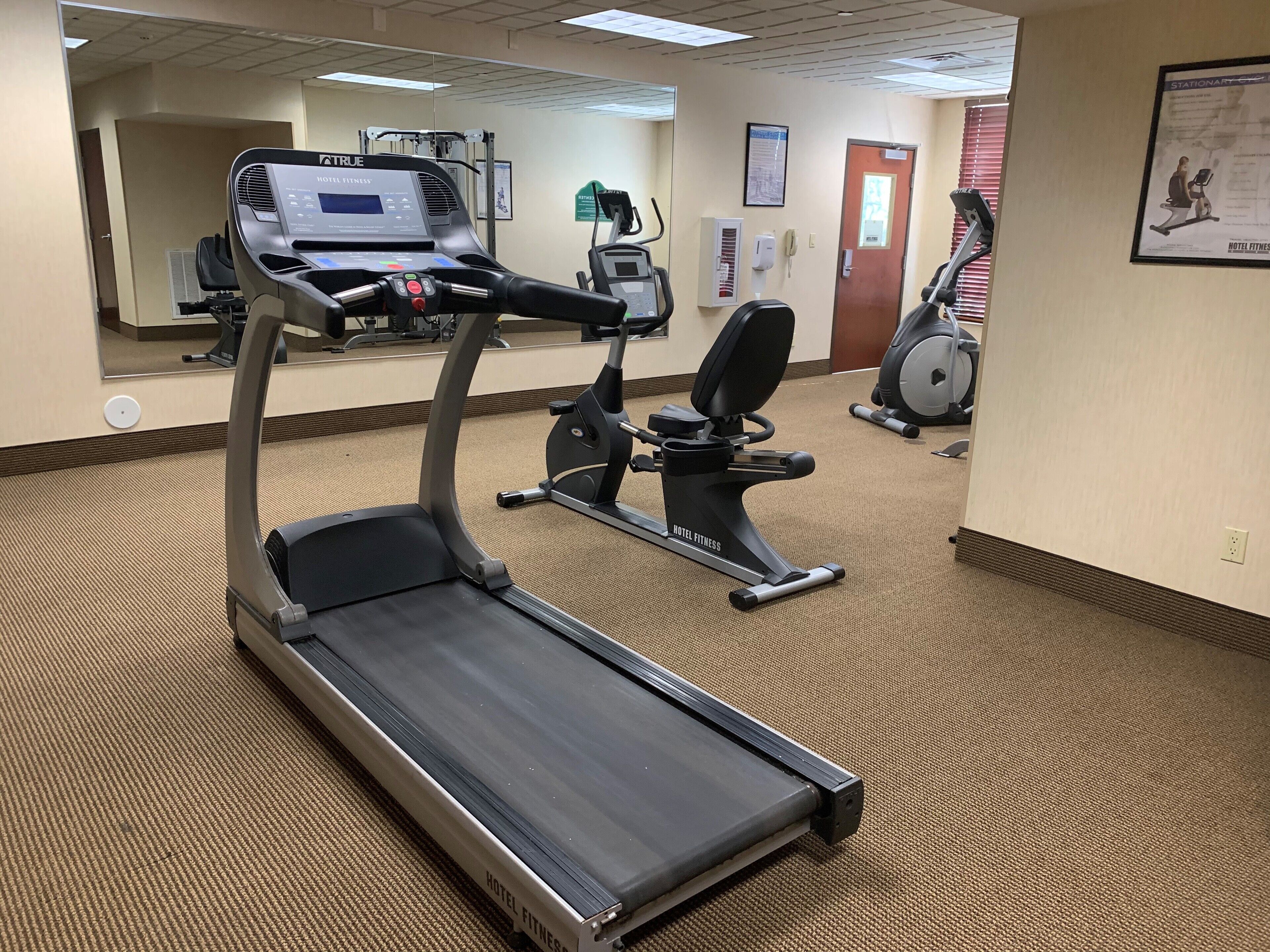 Gimnasio de hotel con cintas de correr, bicicletas estáticas y un espejo grande.