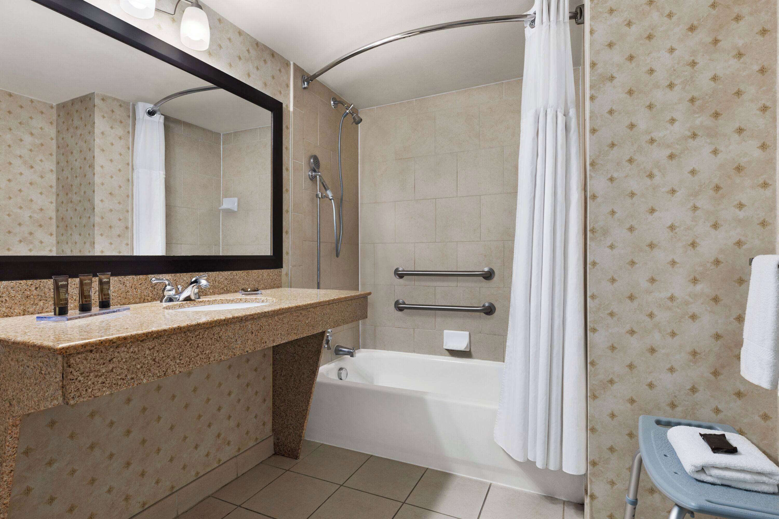 A bathroom with a granite countertop sink, a bathtub, a shower with a curved glass door, and a towel rack.