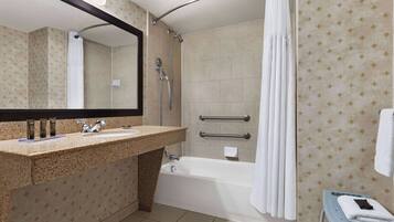 Un baño con lavamanos de encimera de granito, una bañera, una ducha con puerta de vidrio curvada y un perchero para toallas.