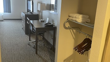 Une chambre d’hôtel équipée d’un bureau, d’une chaise et d’une petite kitchenette. On y trouve une fenêtre avec des rideaux, un téléviseur fixé au mur et un porte-serviettes avec des serviettes.