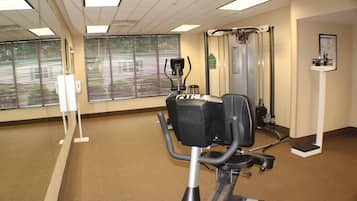 Et fitnesscenter med træningsmaskiner, spejle og vinduer med rullegardiner.