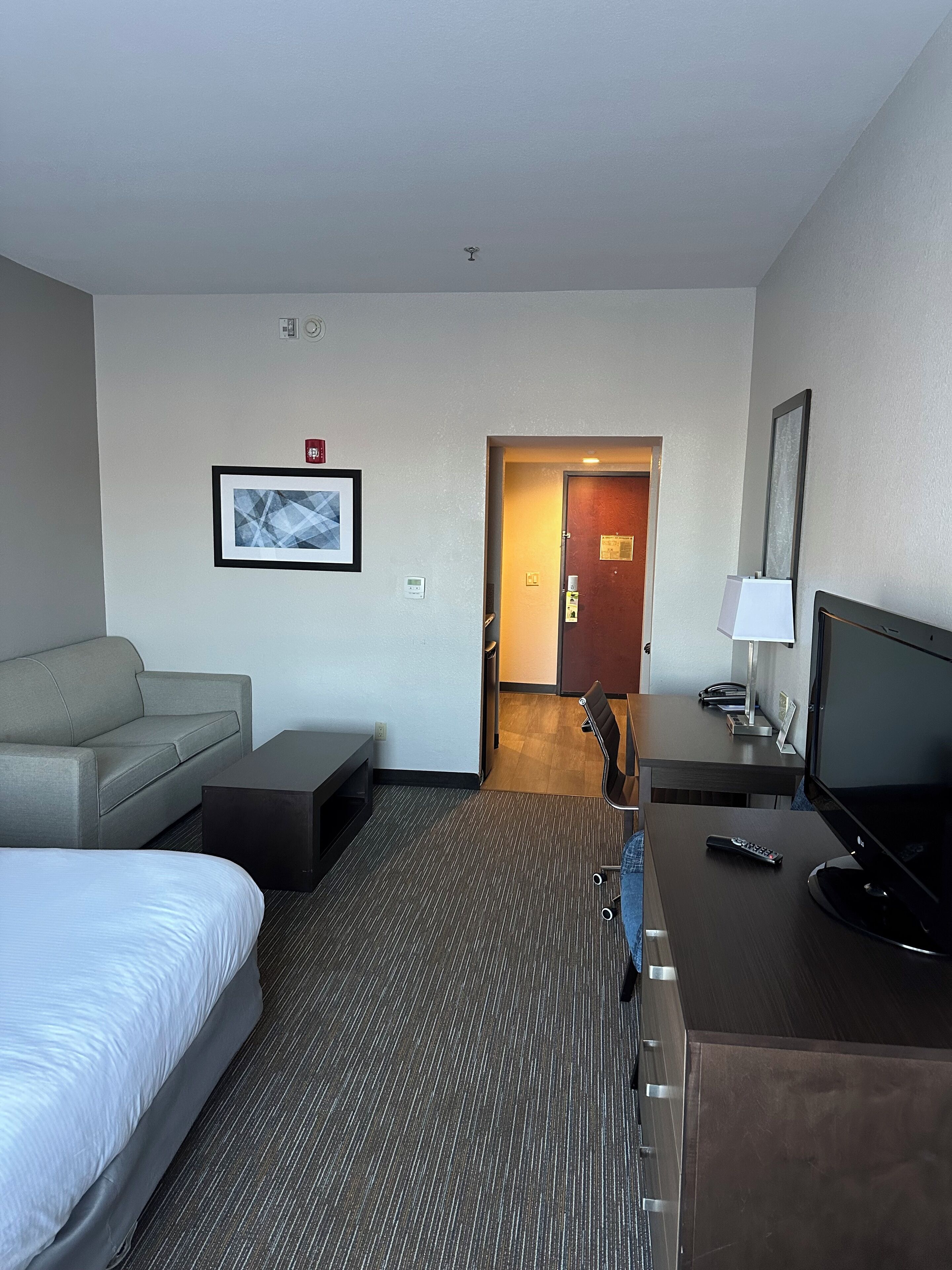 A hotel room with a bed, a sofa, a desk with a TV, a chair, and a door leading to another room.