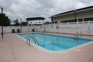 A rectangular swimming pool with a tiled deck, metal ladders, and a covered area with chairs. - Wingate By Wyndham Southport (Southport)