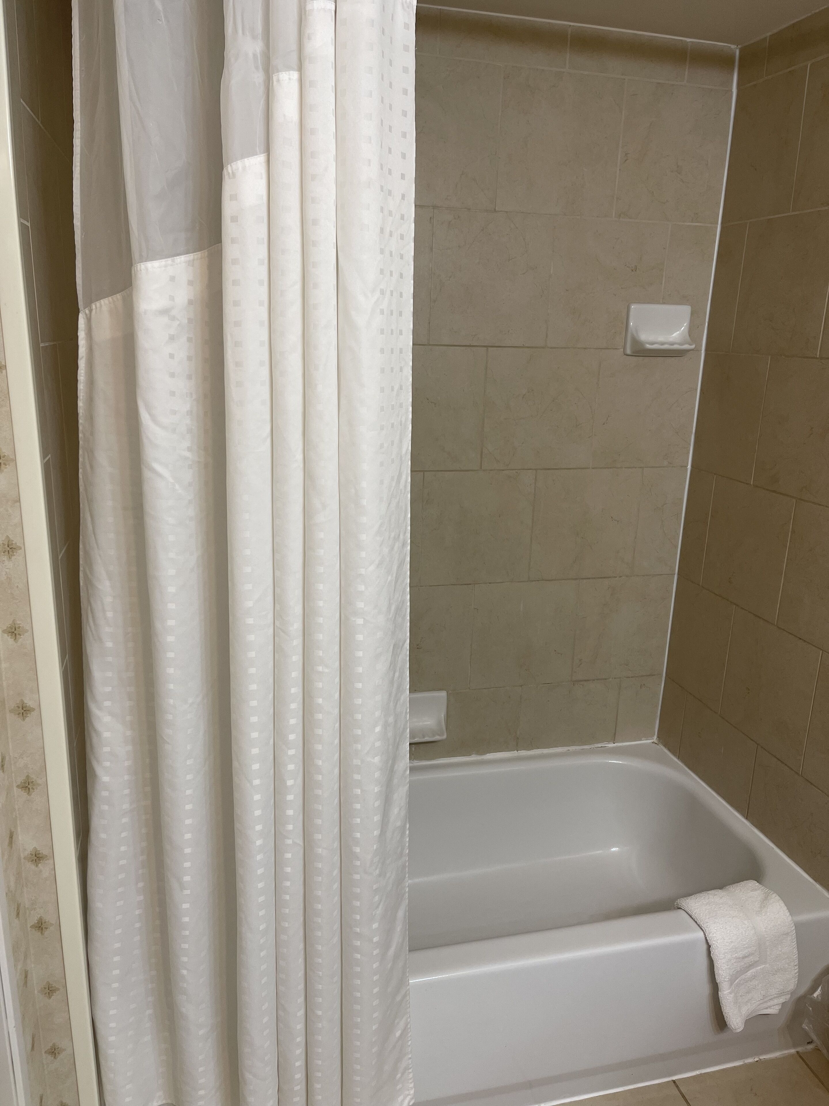 A bathroom with a bathtub, a shower curtain, and beige tiled walls.