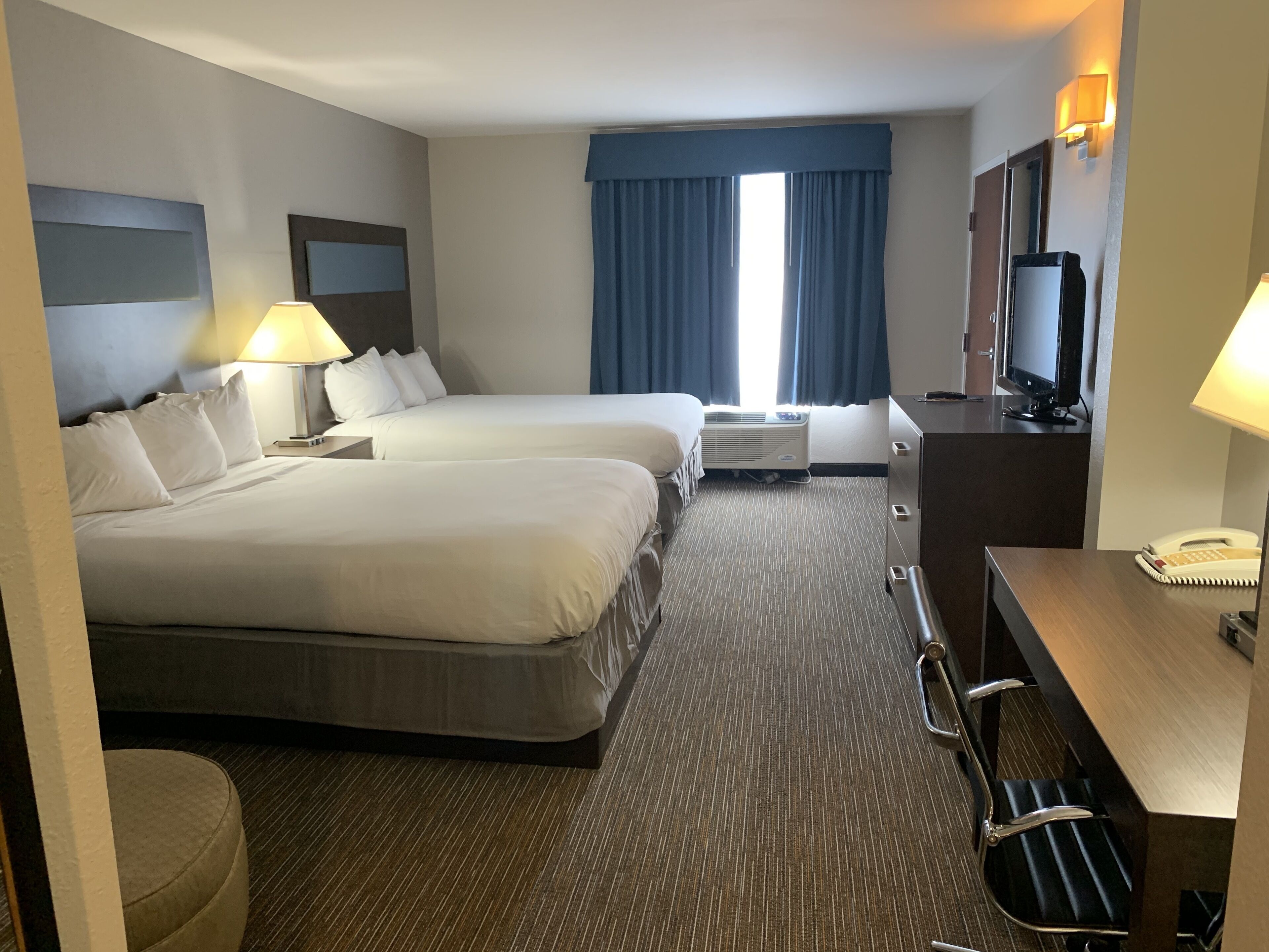 A hotel room with two beds, a desk, a chair, a TV, and a desk lamp.
