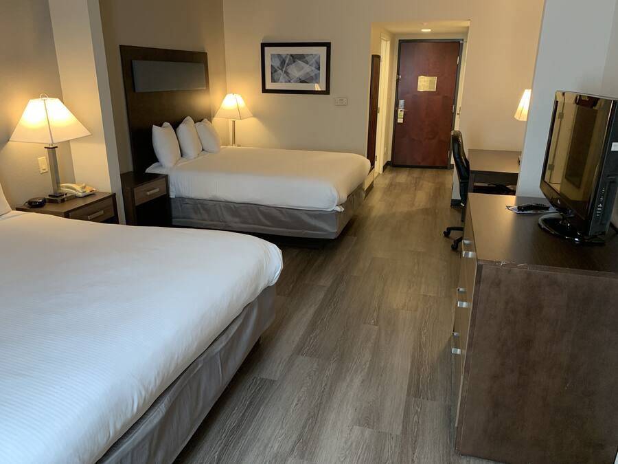 A hotel room with two beds, a desk with a computer, and a door leading to a hallway.